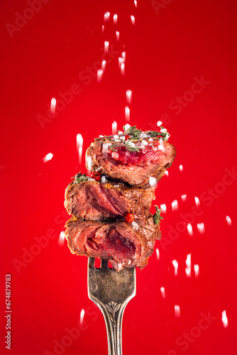 Obraz na plátne Pieces of grill roasted beef meat steak, medium rare, on a fork with spices, salt, herbs and ketchup