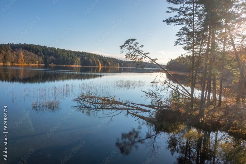 Aerial view on beatiful lake Bolduk in the autumn sunny morning. Woodland and sky are reflected on the water of lake. The wind knocked down trees on the other side of the lake.