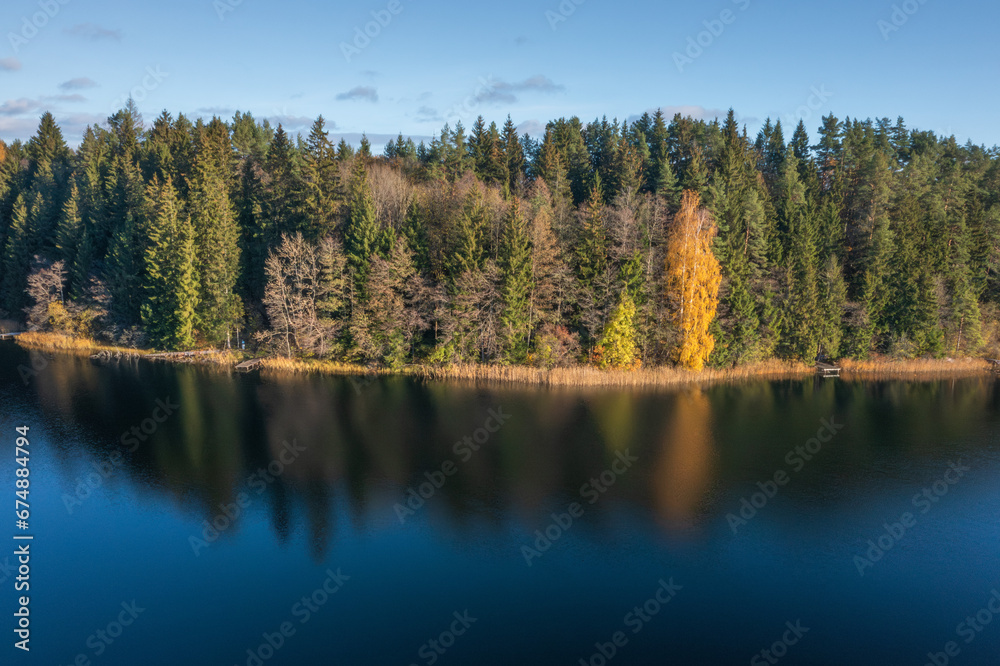 View on picturesque bank of lake in autumn morning, Lake Bolduk. Small wooden piers on the right bank of the lake. The woods is reflected into the water of lake by dark colors.