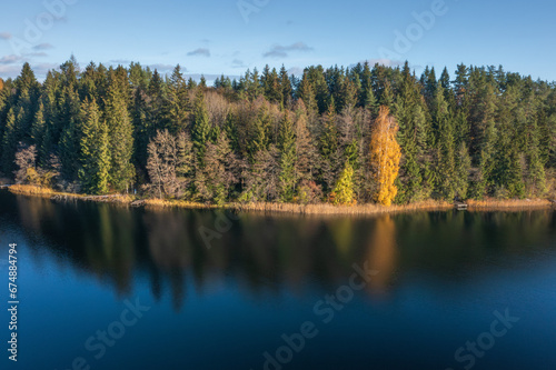 View on picturesque bank of lake in autumn morning, Lake Bolduk. Small wooden piers on the right bank of the lake. The woods is reflected into the water of lake by dark colors.