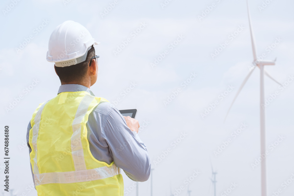 Engineer man stands using tablet front the wind turbines generating electricity power station. .Concept of sustainability development by alternative energy. Engineer man stands using tablet front the wind turbines generating electricity power station. .Concept of sustainability development by alternative energy.