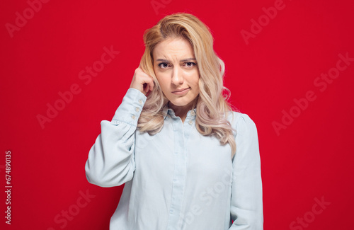 Crafty young woman asking, isolated on red background. Close-up girl at ask concept