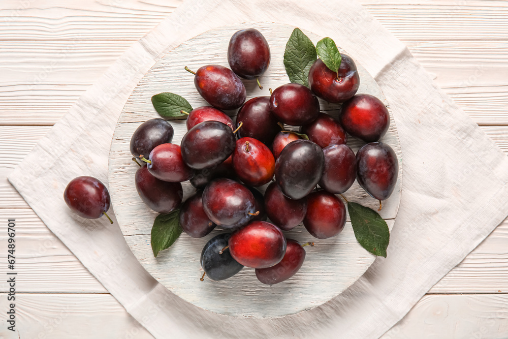 Board with fresh ripe plums and leaves on white wooden background Board with fresh ripe plums and leaves on white wooden background