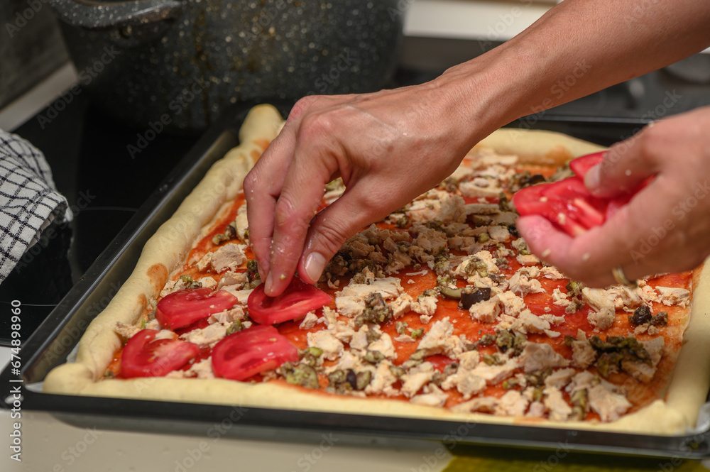 a woman prepares pizza with cheese, tomatoes and chicken ham, a woman lays out tomatoes 1