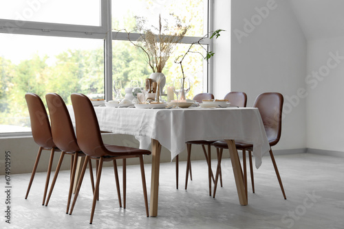 Elegant table setting with dried flowers  candles and plates in light dining room