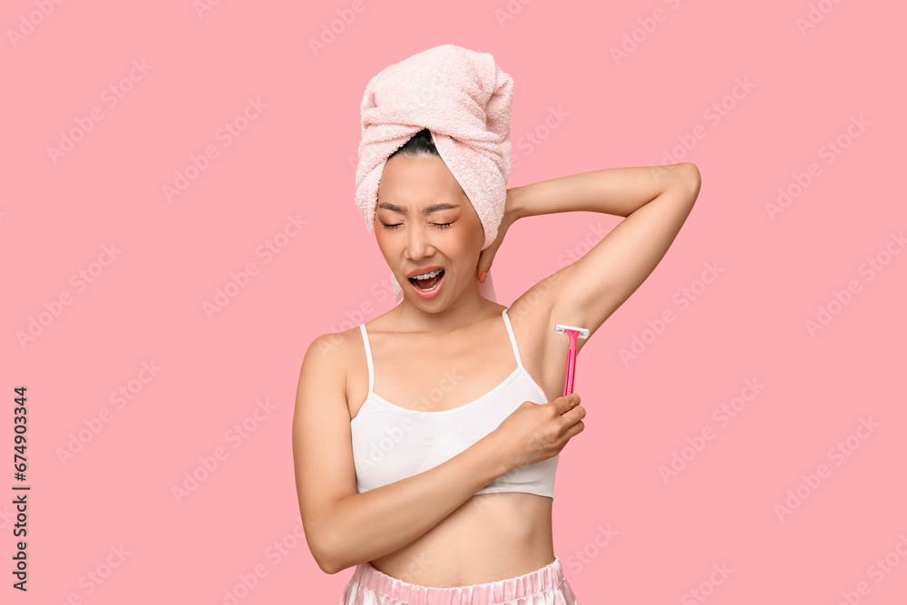 Young Asian woman shaving underarms with razor on pink background Young Asian woman shaving underarms with razor on pink background