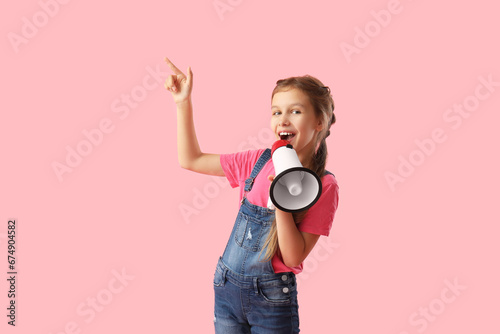 Little girl with megaphone pointing at something on pink background photo