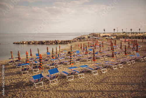 Deserted beach with sunbeds and umbrellas at the Italian Adriatic coast in the preseason, Italy. Closing beach season concept. Selective focus. sandy beach without people. Сlosed sunshade parasols. © Cristina