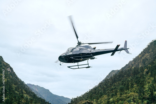 Civil helicopter flying UP in high altitude Himalayas mountains near Kothe settlement, Nepal. Mera Peak climbing  trekking route. Safety air transportation and travel insurance concept image. photo