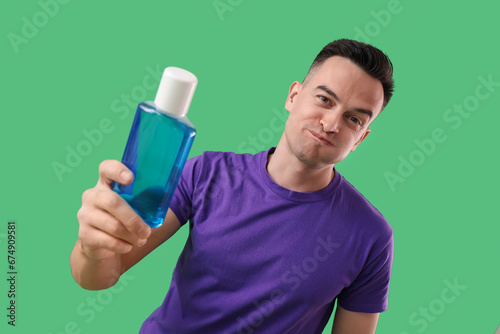 Handsome man with mouth rinse on green background, closeup