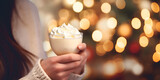 Close up of woman's hands holding a eggnog drink at Christmas market, blurred background with lights 