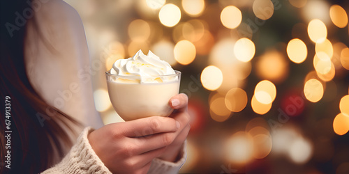 Close up of woman's hands  holding a eggnog drink at Christmas market, blurred background with lights  photo