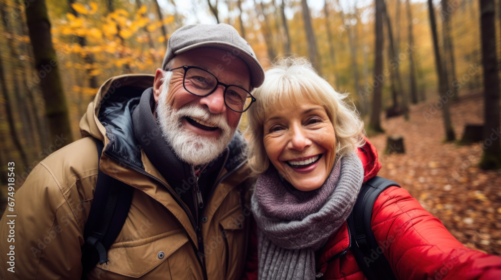 POV portrait of active senior couple looking at camera and smiling while taking selfie photo during hike in autumn forest, copy space