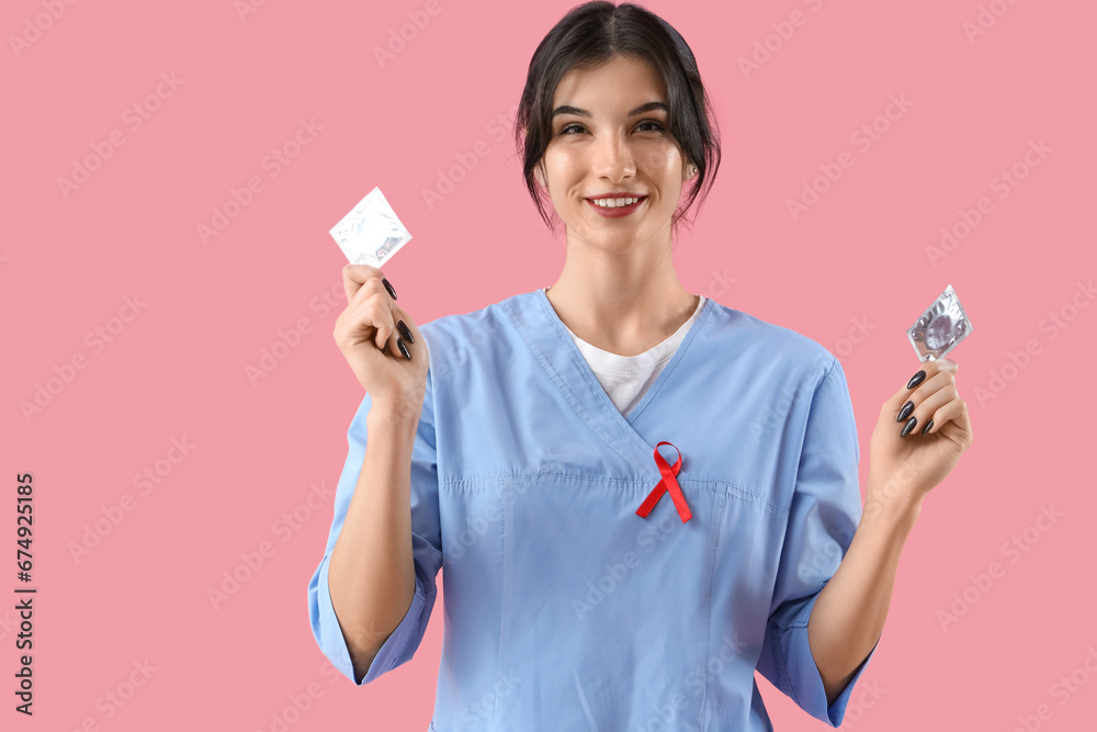 Young female doctor with red ribbon and condoms on pink background. World AIDS day concept Young female doctor with red ribbon and condoms on pink background. World AIDS day concept