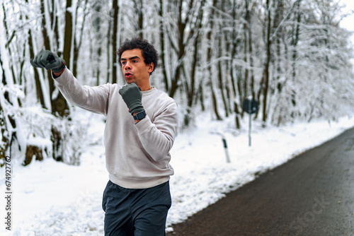 man trains boxing in winter by conducting shadow fight outdoors, in background snow covered forest © DusanJelicic