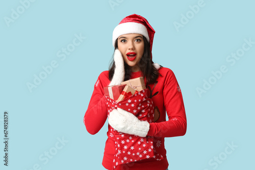 Pretty young woman with bag of Christmas gifts on blue background