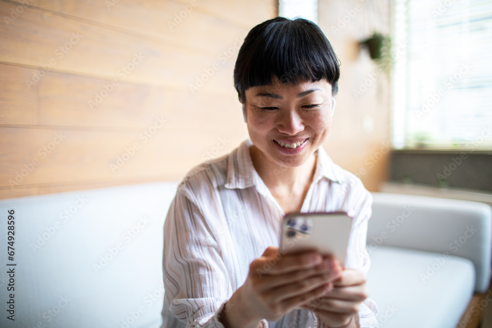 Smiling woman using smartphone on sofa at home Smiling woman using smartphone on sofa at home
