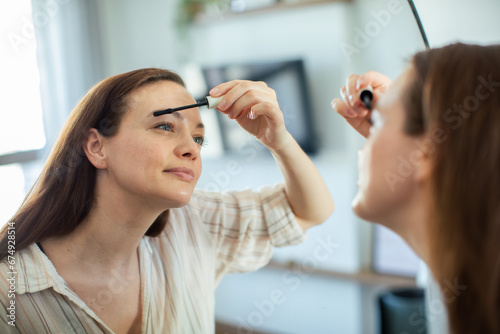 Beautiful young woman applying makeup with help of mirror