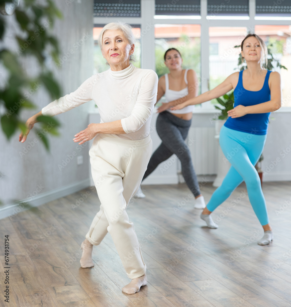 Elderly woman in sportswear performs dance moves in fitness center
