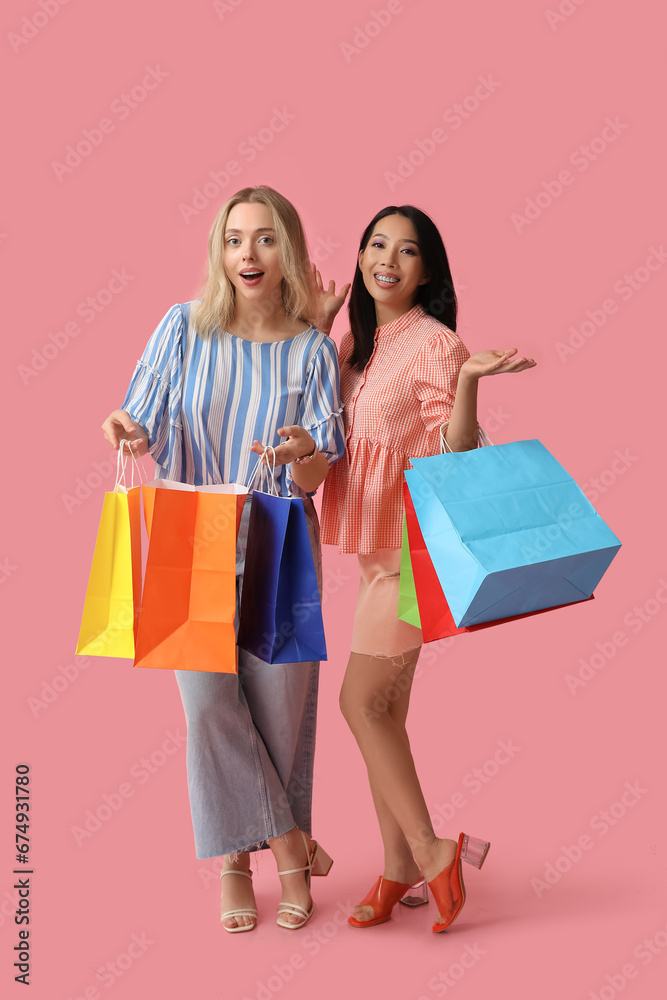 Fototapeta premium Beautiful young women with shopping bags on pink background