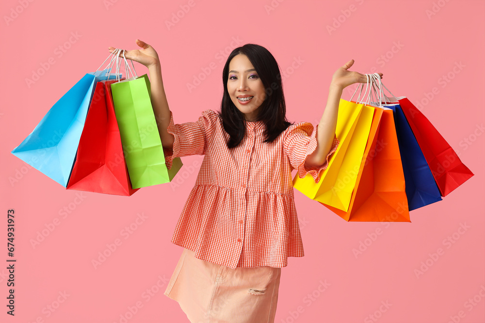 Young Asian woman with shopping bags on pink background