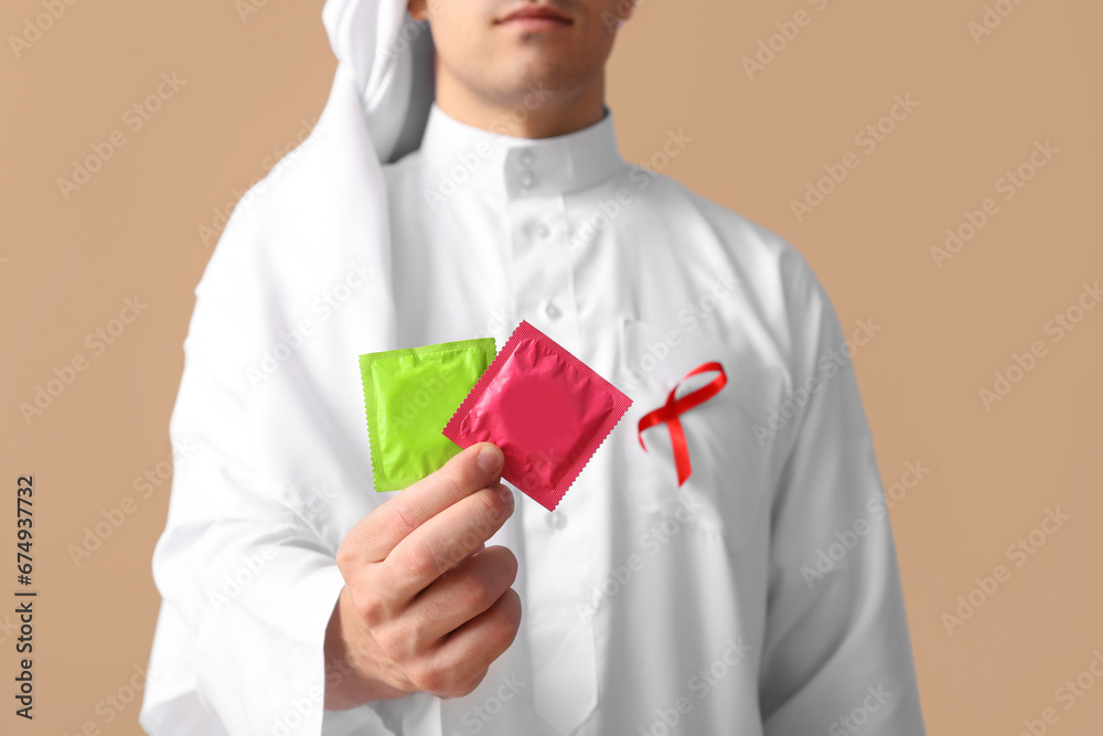Handsome Muslim man with red ribbon and condoms on brown background. AID awareness concept Handsome Muslim man with red ribbon and condoms on brown background. AID awareness concept