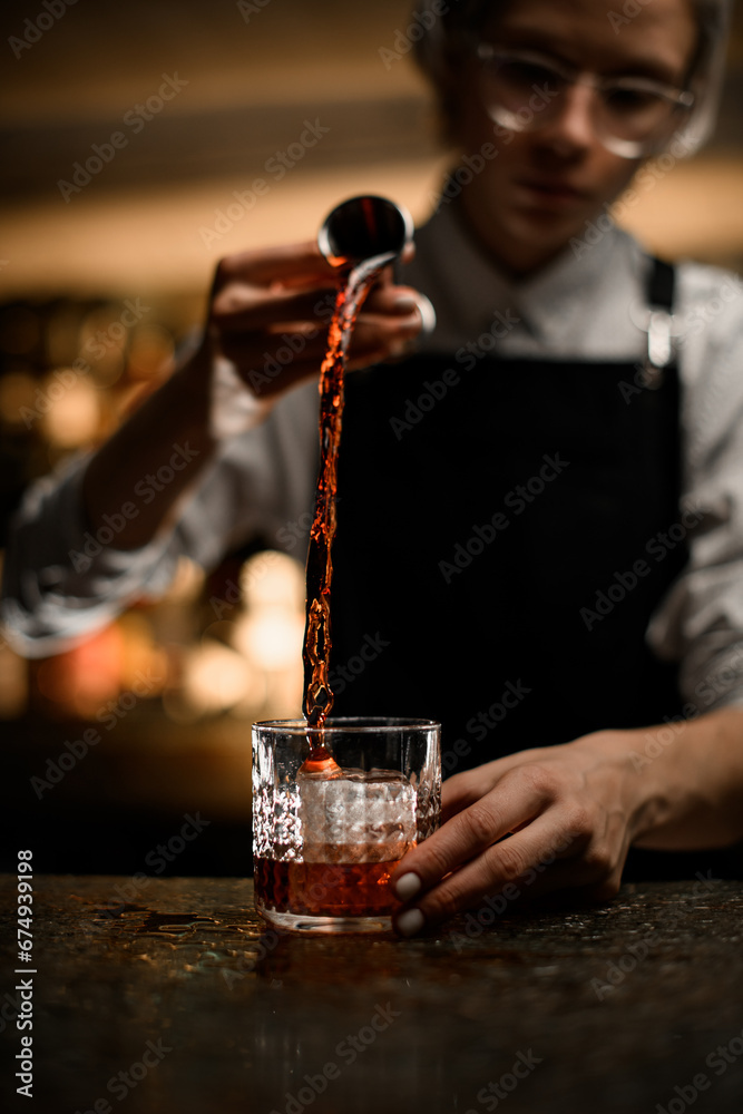 Female bartender pouring an alcoholic drink into a glass for making a cocktail
