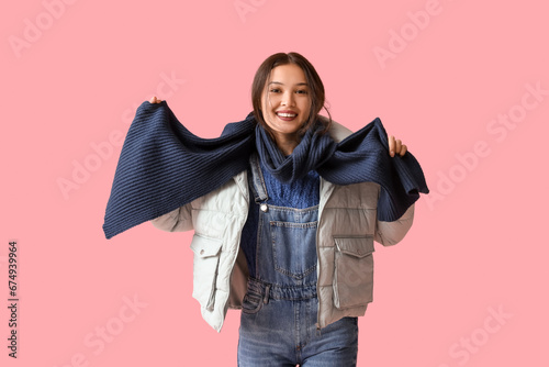 Beautiful young Asian woman in warm scarf on pink background