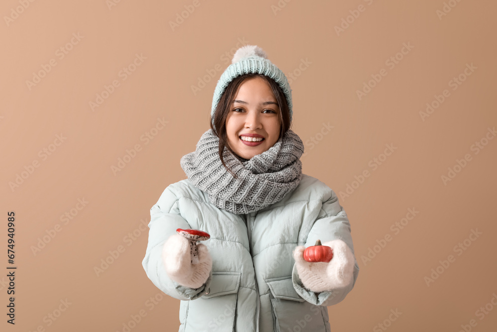 Beautiful young Asian woman in warm scarf with decorative toys on brown background