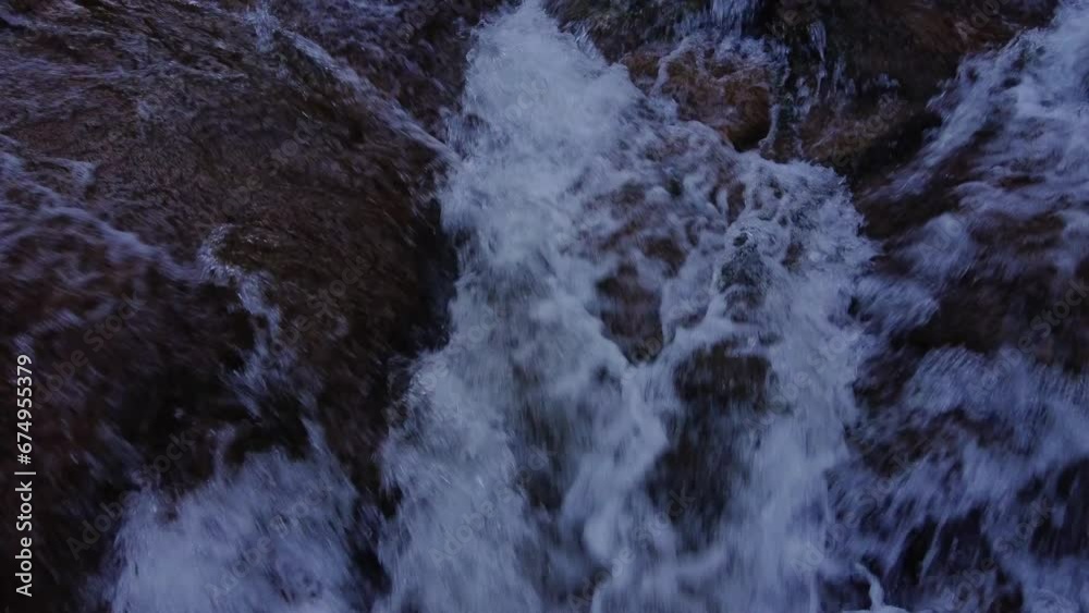 A close-up aerial view of a mountain river with white splashes of water cascading down a rocky shore. A mountain river with fast-flowing water A close-up aerial view of a mountain river with white splashes of water cascading down a rocky shore. A mountain river with fast-flowing water