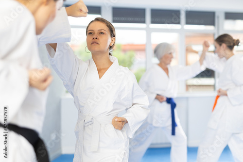 Concentrated young woman in kimono honing punching techniques during kumite with female opponent at karate training session