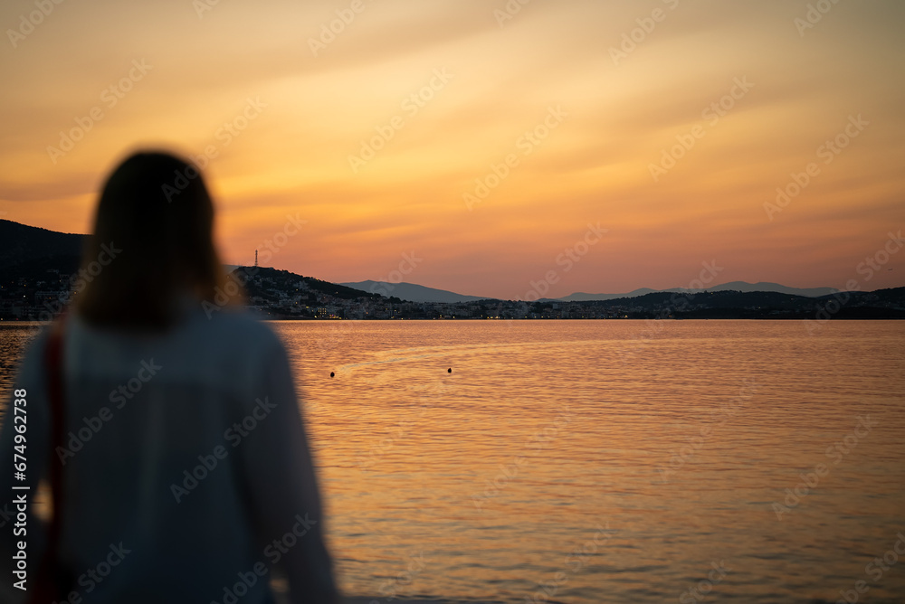 Woman looks at the city of Porto Rafti at sunset.