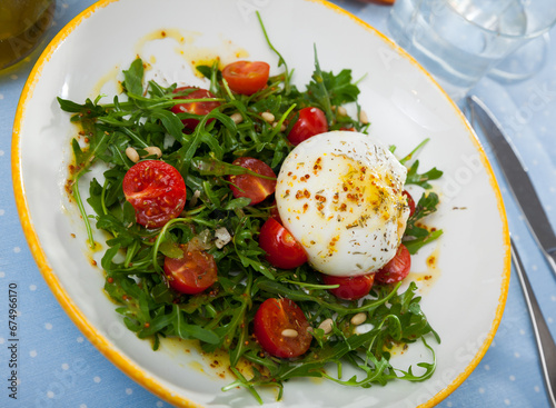 Colorful salad with Italian cow milk cheese burrata on pillow of fresh rocket with cherry tomatoes..