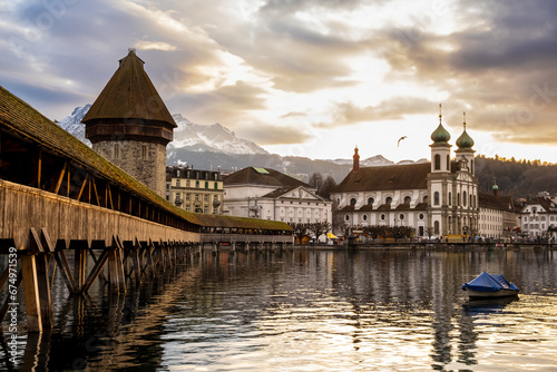 Old town of Lucerne, Switzerland at sunset in winter. Famous wooden Chapel Bridge on Reuss river, Jesuit Church, snowcapped mountain. Swiss historic buildings and medieval architecture near water