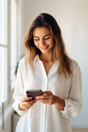 A woman in shirt looking at mobile phone in bright bedroom