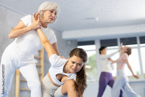 Elderly woman and young woman training self-defense techniques in group in studio