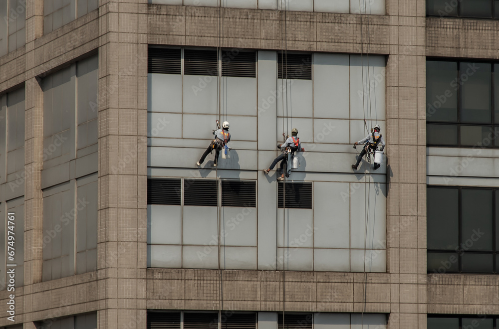 Group of workers cleaning windows service on high rise office building with reflection from swimming pool. Selective focus.