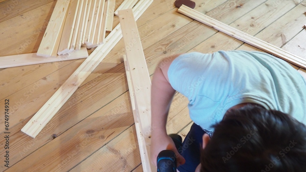 Young teenager boy assembling furniture at home. boy using a screwdriver tool assembles parts of wooden furniture, shelving. interior, cozy home, help for parents Young teenager boy assembling furniture at home. boy using a screwdriver tool assembles parts of wooden furniture, shelving. interior, cozy home, help for parents
