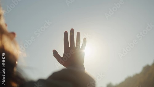 Hand of young woman at sunset close-up. Sun between the hands of tourist woman. Silhouette of happy dreaming female pulls her hand to the sun photo