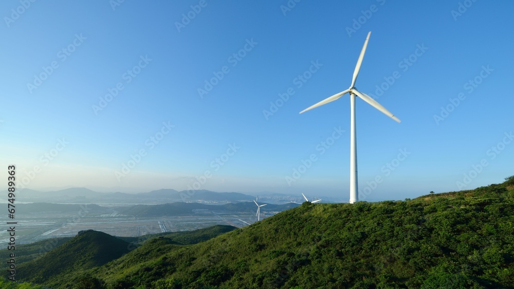 White wind turbines atop a mountain peak with a bright blue sky in the background White wind turbines atop a mountain peak with a bright blue sky in the background
