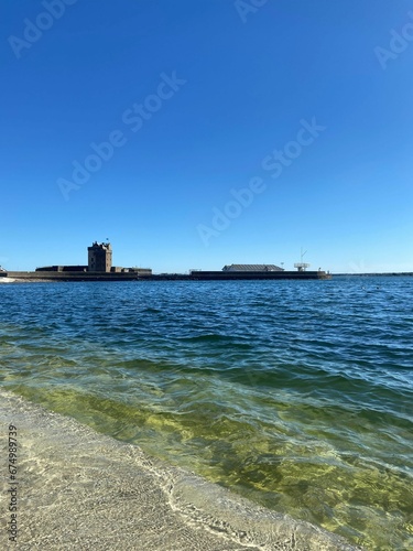 Serene shoreline of a tranquil sea with buildings in the background © Wirestock