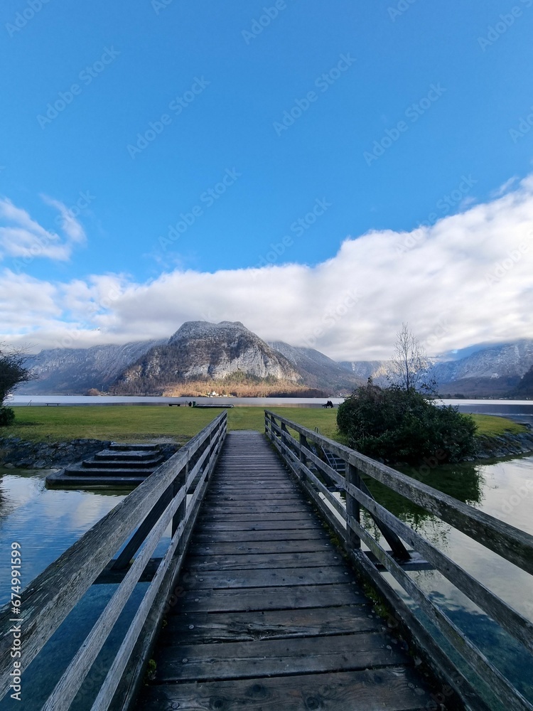 Rustic wooden bridge spanning a tranquil blue lake on a sunny day, providing a tranquil pathway