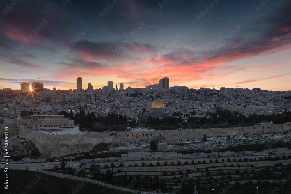 sunset over the dome of the rock with buildings and green lawn below