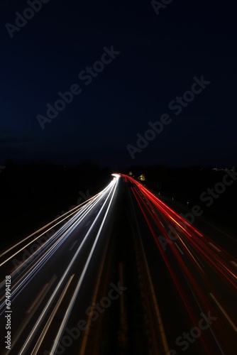 Vertical long exposure shot of glowing car lights on a dark highway
