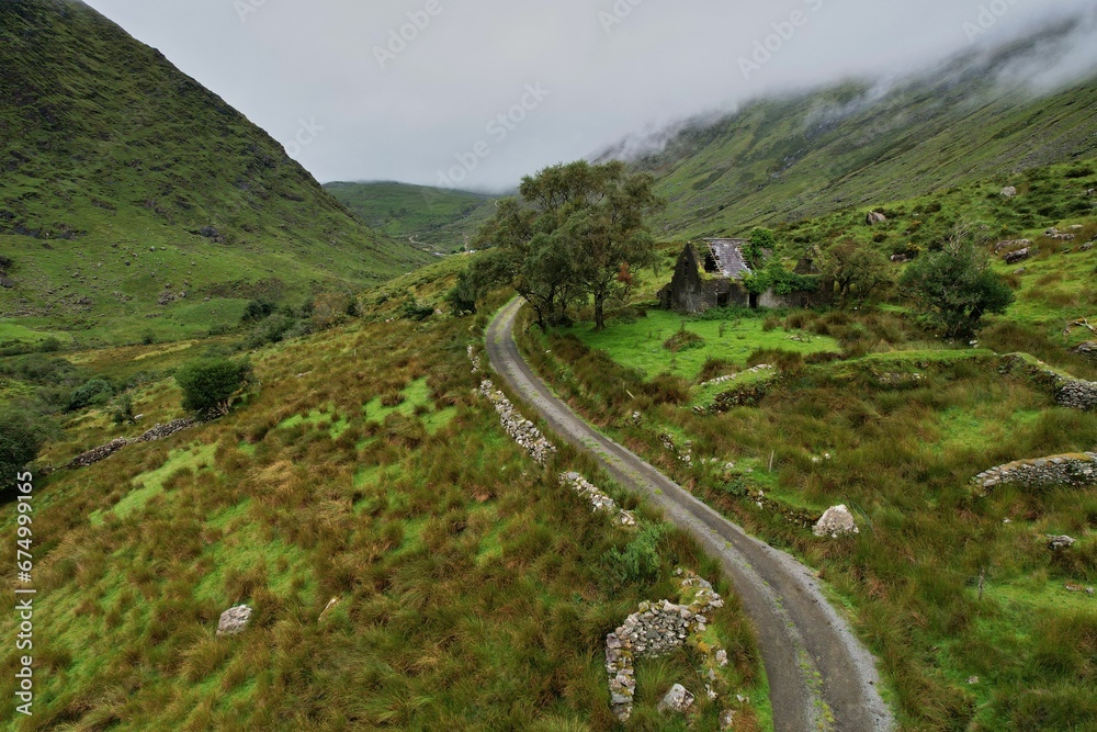 Fototapeta premium Aerial view of Molly's Cottage in County Kerry, Ireland, surrounded by lush green hills