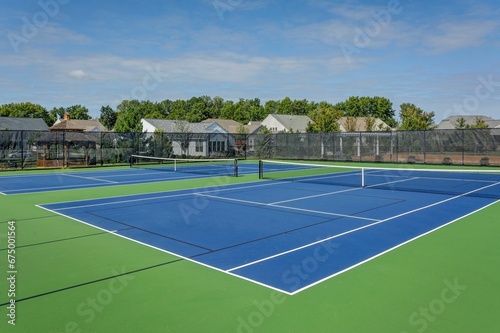two tennis courts are located within a fenced area and surrounded by homes photo