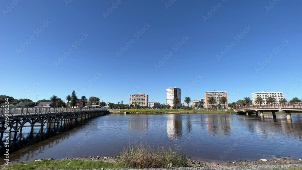 Pedestrian bridge crossing next to road bridge at a river lined with palm trees and high rise apartments on a sunny day Pedestrian bridge crossing next to road bridge at a river lined with palm trees and high rise apartments on a sunny day