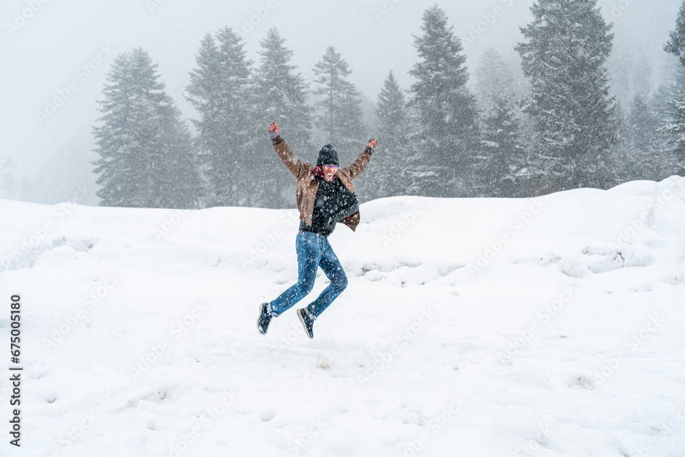 Single Asian man tourist having fun, excitement, jumping, happy in middle of snow falling, View of Sonmarg Valley in Himalayas, weather was white and snowy in winter. Sonamarg, Jammu, Kashmir, India