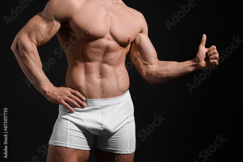 Young man in stylish white underwear showing thumb up on black background, closeup