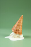 Melted ice cream and wafer cone on green background, space for text